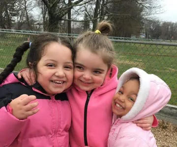 three girls in jackets smile on playground